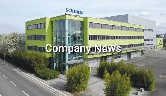 Image with the caption Company news in front of a photo of the SCHUKAT company building with a green facade and glass front. The image refers to current news from the company.